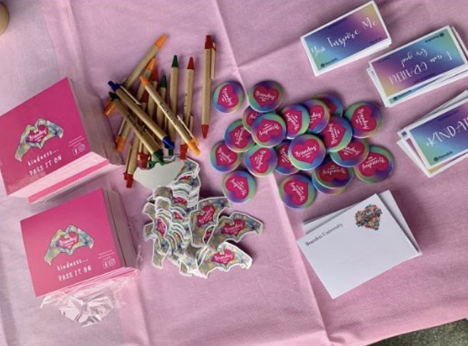 Kindness Day giveaway table with sticky notes, stickers, buttons, pens, and gradient cards